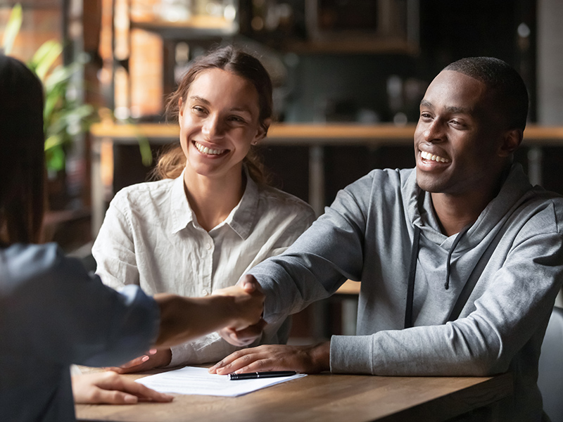 Happy, smiling interracial couple shaking hands with financial advisor, discussing commercial loans