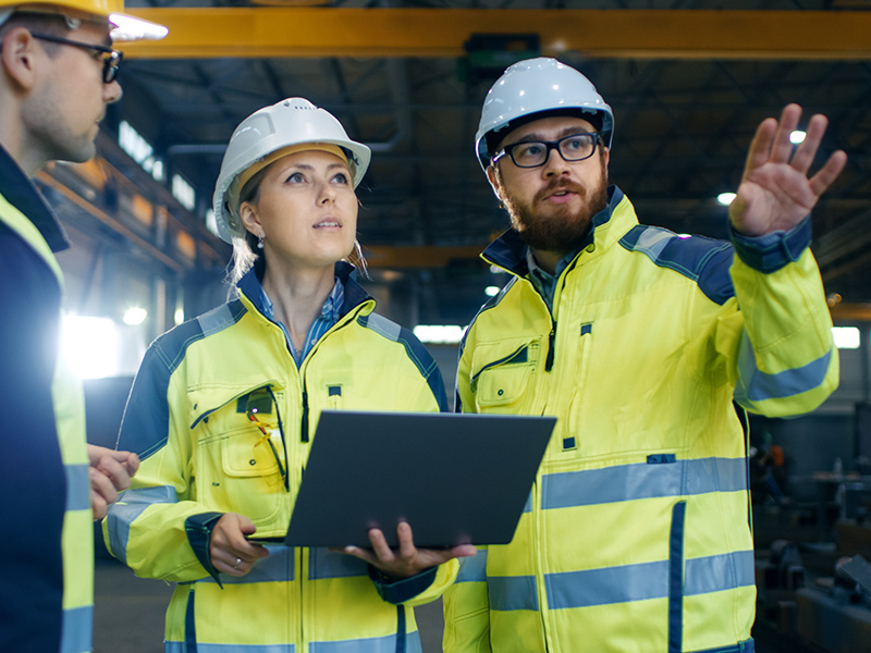 Three suppliers in warehouse discussing finance and using laptop