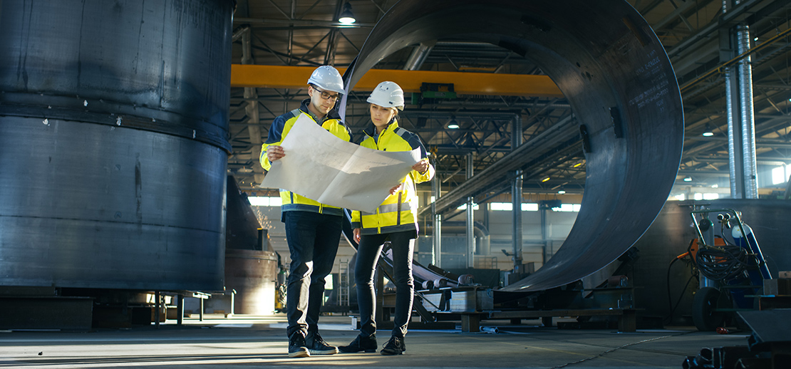 Male and female warehouse manufacturers looking at documents to work out financial funding options