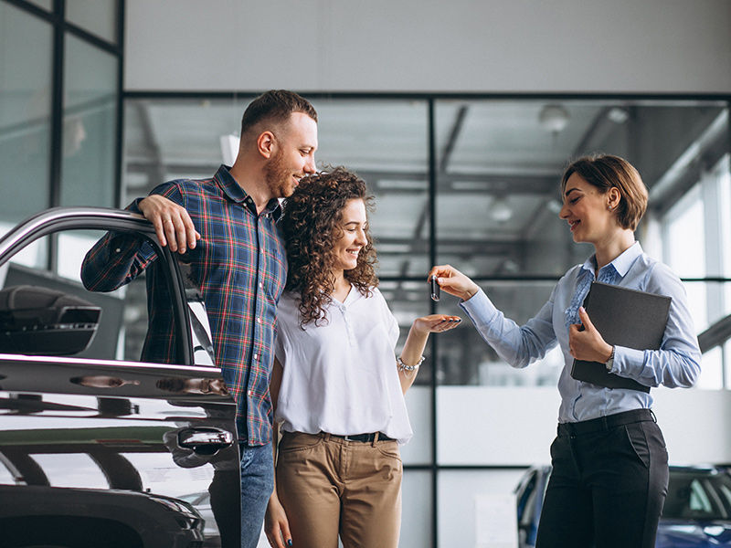 Happy couple being handed over car keys by an advisor to be hired for personal use